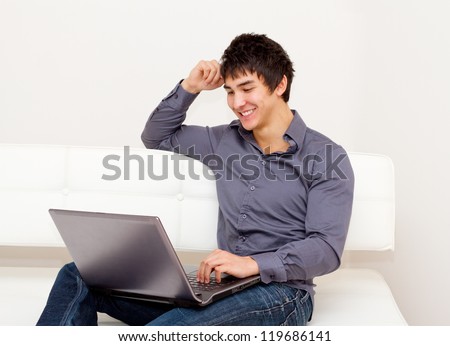 Handsome smiling man sitting comfortable on the sofa. Surfing the net, using a laptop.