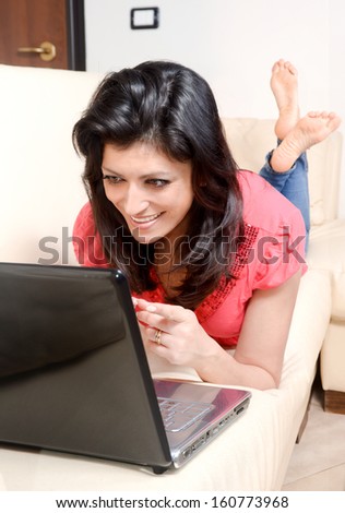 smiling young woman lying on the couch, surfing the internet with her laptop computer. Concept of relaxation