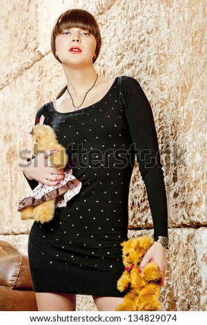 Girl with bangs in a black dress posing with teddy bears