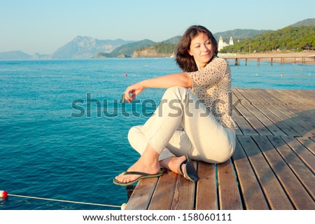 girl sitting on a pier near the sea and looking to the side