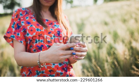 Charming young woman using to mobile smart phone, against green of summer