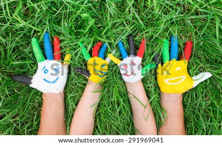 Colored hands with smile painted in colorful paints against green summer background. Lifestyle concept