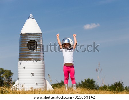 Happy child dressed in an astronaut costume playing with hand made rocket. Summer outdoor
