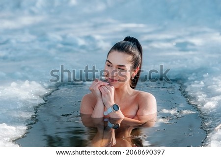 Girl with bikini and a watch in frozen lake ice hole. Woman hardening the body in cold water. Good immunity is protection against many diseases. Vintage color filter 商業照片 © 