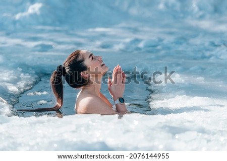 Girl with bikini and a watch in frozen lake ice hole. Woman hardening the body in cold water. Good immunity is protection against many diseases. Vintage color filter 商業照片 © 