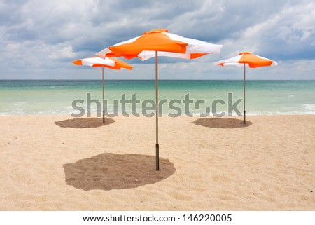 Beach umbrellas on the white sand beach with cloudy blue sky and sun