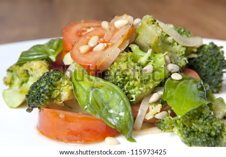 Fresh broccoli salad with lettuce, bell pepper, pine nuts,  tomatoes and onion on a white plate, which stands on a wooden table(Selective Focus, Focus on the broccoli floret in the front)