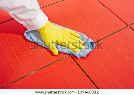 Hand with yellow gloves and blue towel clean red tiles grout