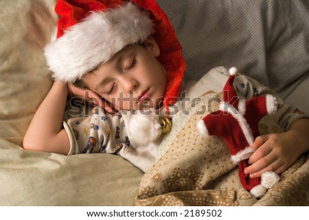 Little boy in Santa\'s hat sleeping with a toy in a hand