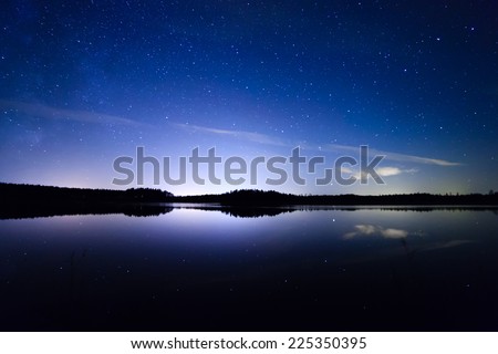 Stars and night clouds with reflections over the lake at night in Finland.