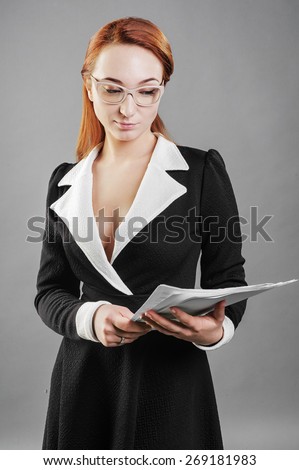 Girl standing on a gray background in the hands of paper, black dress, glasses, business style,