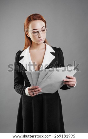 Girl standing on a gray background in the hands of paper, black dress, glasses, business style,