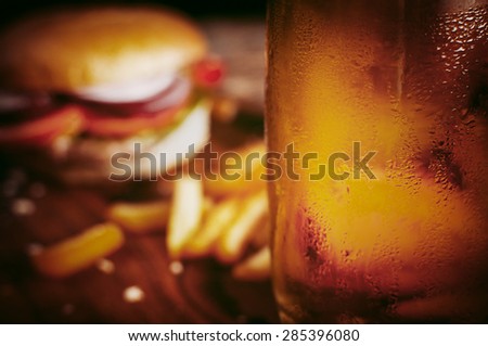 Glass of ice cold beer in front of french fries and burgher served on wooden board