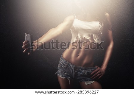 Young fitness woman taking a selfie of her shaped body ready to share it on social media