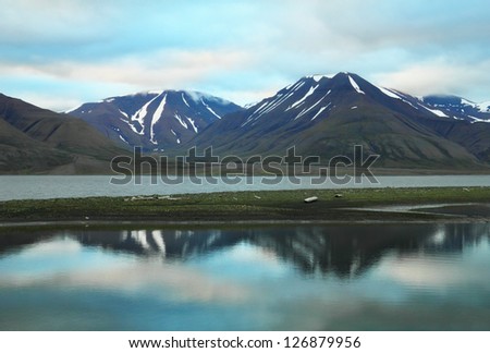 Scenic view of black rocks with melting snow and colorful dramatic sky reflected in calm water of Advent Bay near Longyearbyen, Norway, Spitsbergen archipelago (Svalbard island), Norway, Greenland sea