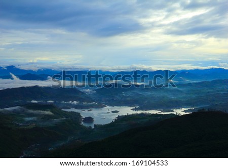 Beautiful scenic view at early morning - shadow figures of fogged mountain tops and serene lake against the background of dramatic blue sky near Sri Pada (Adam\'s Peak), Sri Lanka island, South Asia