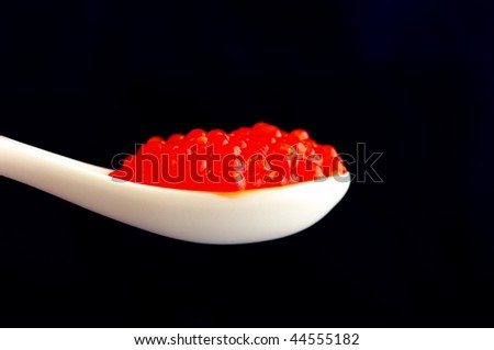 spoon full of red caviar against black background