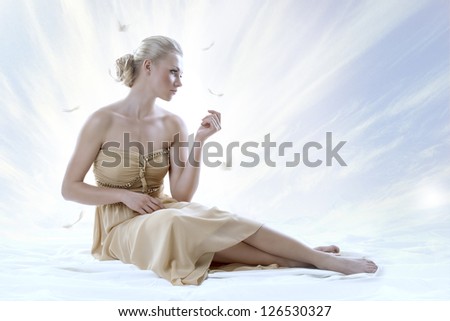 pretty blonde girl with elegant dress sitting on white floor, with a sky as a background, her face is turned at left and she looks in front of her