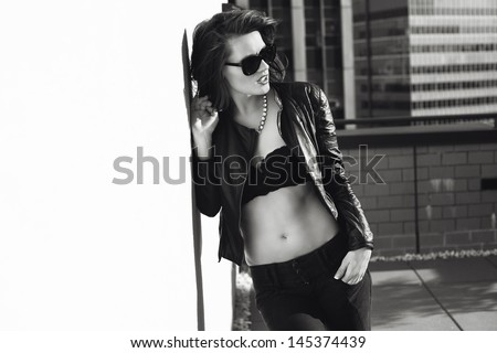 Glamorous young woman in black leather jacket and sunglasses on the rooftop