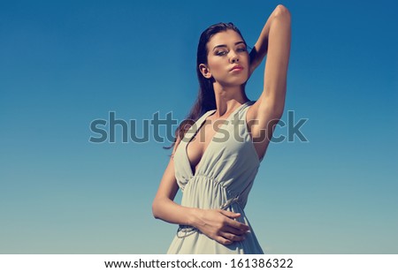 Portrait of beautiful brunette woman wearing dress against blue sky