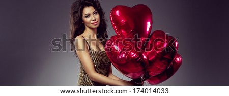 Beautiful brunette young woman in golden dress with a heart-shaped balloons