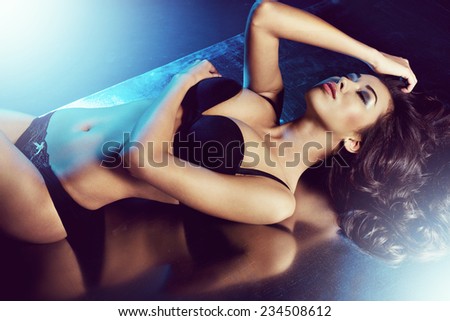 sexy woman posing in black sensual lingerie with blue light coming from behind. Fashion shot