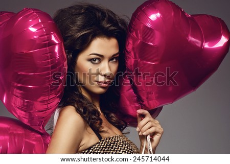 sexy brunette young woman in golden dress with a heart-shaped balloons