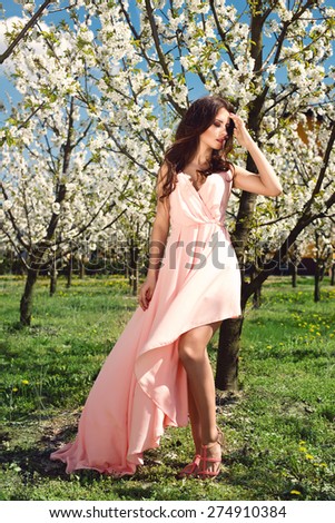 outdoor portrait of a beautiful brunette woman in pink dress among blossom cherry trees. Fashion photo