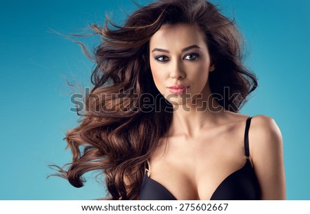 portrait of sexy brunette woman with a perfect body and large breasts posing in black lingerie on a blue studio background