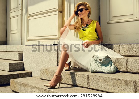 Beautiful blonde young woman wearing fashionable clothes sitting on stairs
