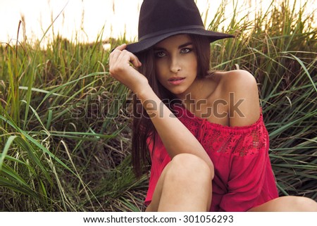 young beautiful woman in jeans shorts, red top and black hat on a field in summer. Fashion photo on a meadow.