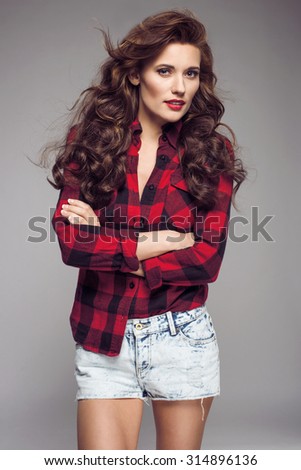 Portrait of young sexy woman in jeans shorts, red checked shirt, red lips. Fashion studio shot.