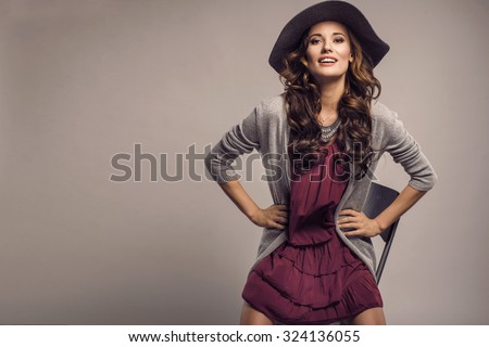 Fashionable woman in a hat, dress and long grey sweater, posing in studio. Fashion autumn photo
