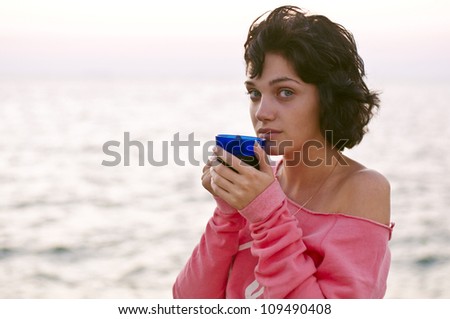 young woman drinks tea near the sea
