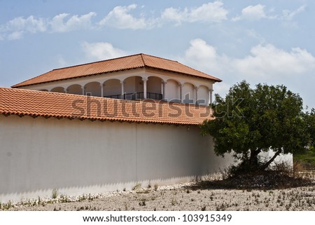 Exterior of a modern building with tiled roofs and covered arcades . It is stylized to classical Spanish style. White columns, red tiles, olive tree, blue sky. Caesarea, Israel.