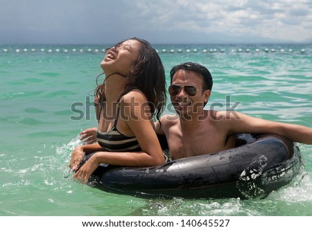 A teenage Filipino girl and her male cousin laughing and enjoying themselves playing with an inner tube swimming in the ocean.