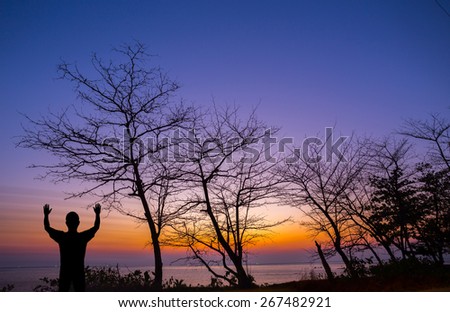 Silhouette man show his hand up in the air with dead tree at sunset beach