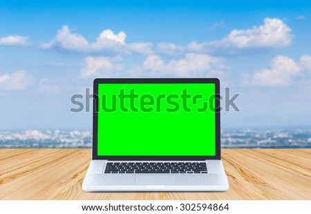 Green screen laptop computer on wood table and clouds blue sky background