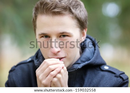 Young man warming hands with breathe, outside cool weather