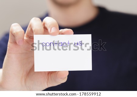 adult man hand  holding card contact us in front of camera, blurred background