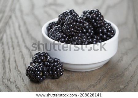 ripe blackberries and raspberries in white bowl on old oak table, rustic style