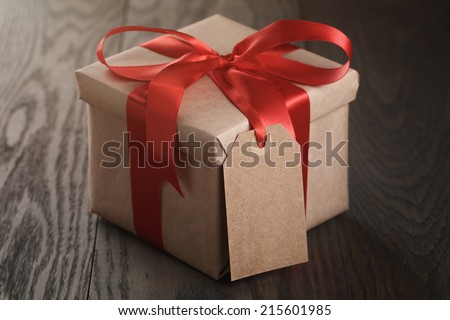 rustic gift box with red ribbon bow and empty tag, on old wood table