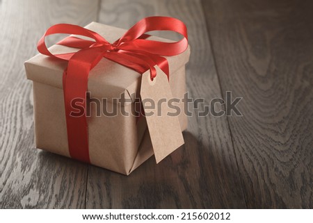 rustic gift box with red ribbon bow and empty tag, on old wood table