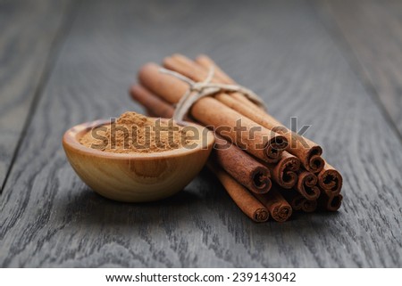 bunch of cinnamon sticks tied with twine and powder in bowl, on rustic oak table