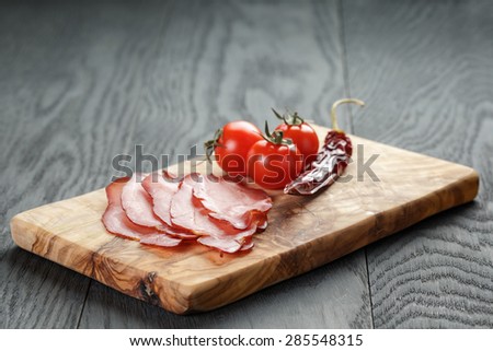 smoked ham prsut with cherry tomatoes and chili, on wooden table