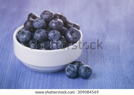 fresh blueberries in bowl on blue wood table, vintage toned