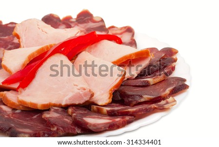 Sliced homemade dry sausages and meat products, cured meat, with slices of fresh bell pepper on a white plate. Isolated on white background, close-up.