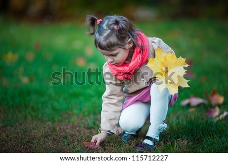 Toddler girl pick up leaves in the park