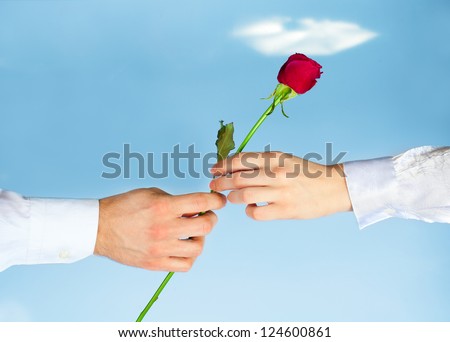 Hands of man giving rose to woman on blue sky background