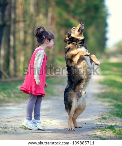 Happy little girl playing with big staying \
dog in the forest